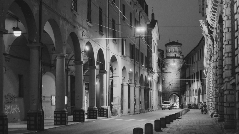 Evening falls on the warm, historic porticoes of Bologna, Italy, lit by golden streetlamps and steeped in charm.