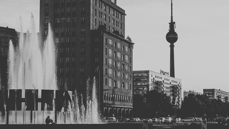 Photo of Berlin captures the Fernsehturm (TV Tower) rising above modernist buildings and a fountain scene in the foreground