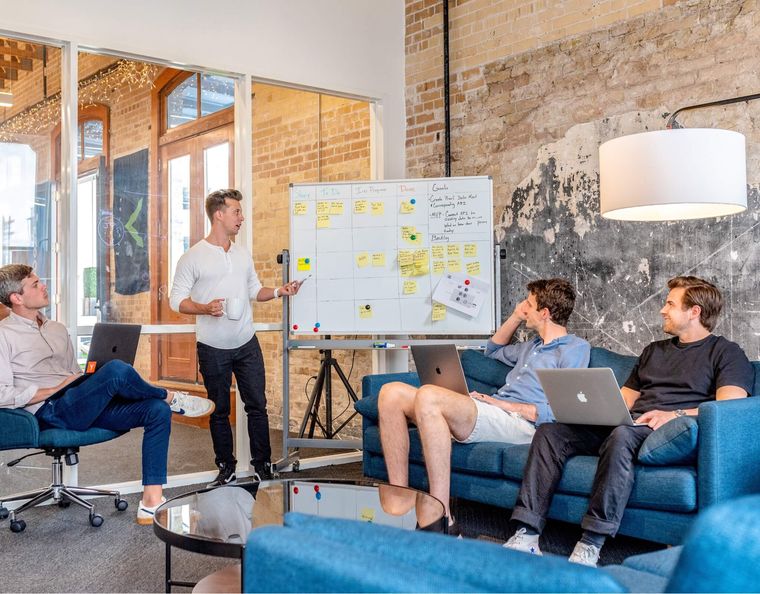 Man standing at whiteboard presenting to three team members sitting to either side of him